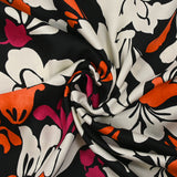 Fine viscose satin printed with fuchsia, orange and ecru royal flowers on a black background