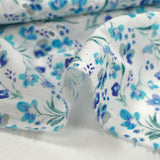 Bordado inglés estampado con pequeñas flores azules sobre fondo blanco.