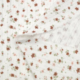 Punto pointelle de algodón estampado con un vuelo de flores rosas y ladrillo sobre un fondo blanquecino